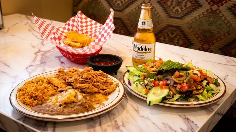Mexican meal with shredded chicken, rice, beans, salad, chips, salsa, and a Modelo beer.
