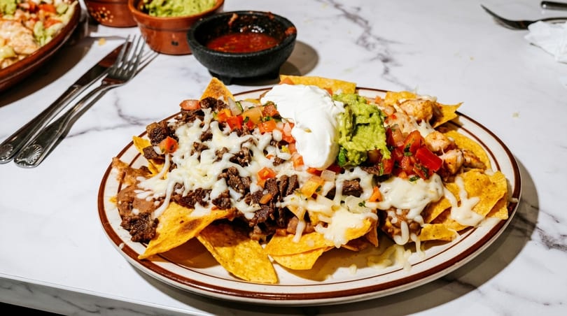 A plate of loaded nachos with beef, chicken, cheese, guacamole, sour cream, and salsa.